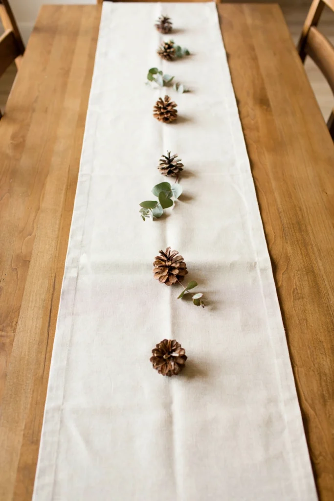 Natural linen table runner styled with pinecone clusters for a Scandinavian Christmas table