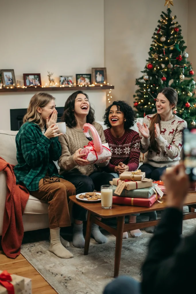 Pile of wrapped gag gifts on a coffee table with friends laughing during a White Elephant gift exchange