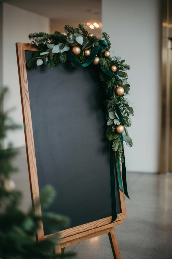 Large chalkboard easel with hand-lettered welcome message and company name, styled with a greenery swag