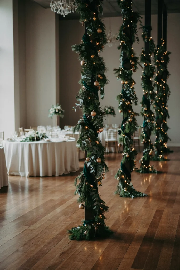 Structural pillars in a rented ballroom wrapped in spiraling greenery garland from base to top