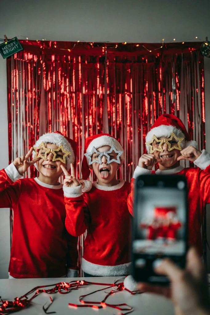 Kids posing in Santa hats and glitter glasses in front of a shimmering red metallic fringe photo backdrop