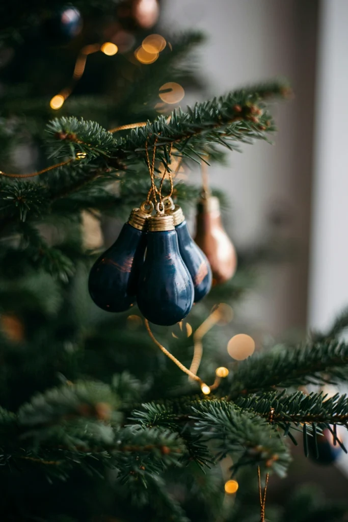 Hand-painted light bulb ornaments in matte navy and copper hanging from a tree branch