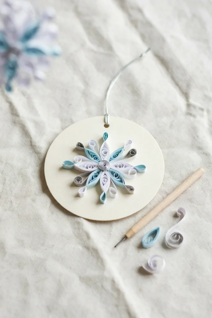 Delicate quilled snowflake ornament made from tightly rolled strips of white and silver paper with intricate three-dimensional swirls and spirals