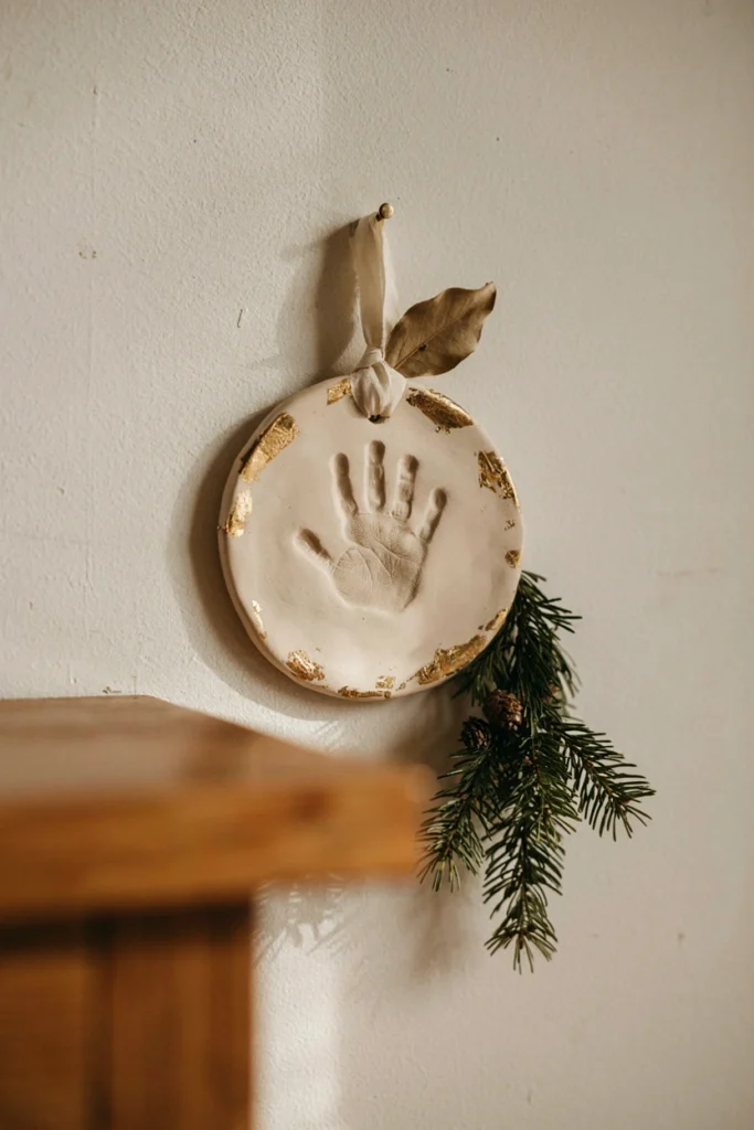 Round gold-painted air-dry clay disc with a deep handprint impression hanging on a wall by a ribbon