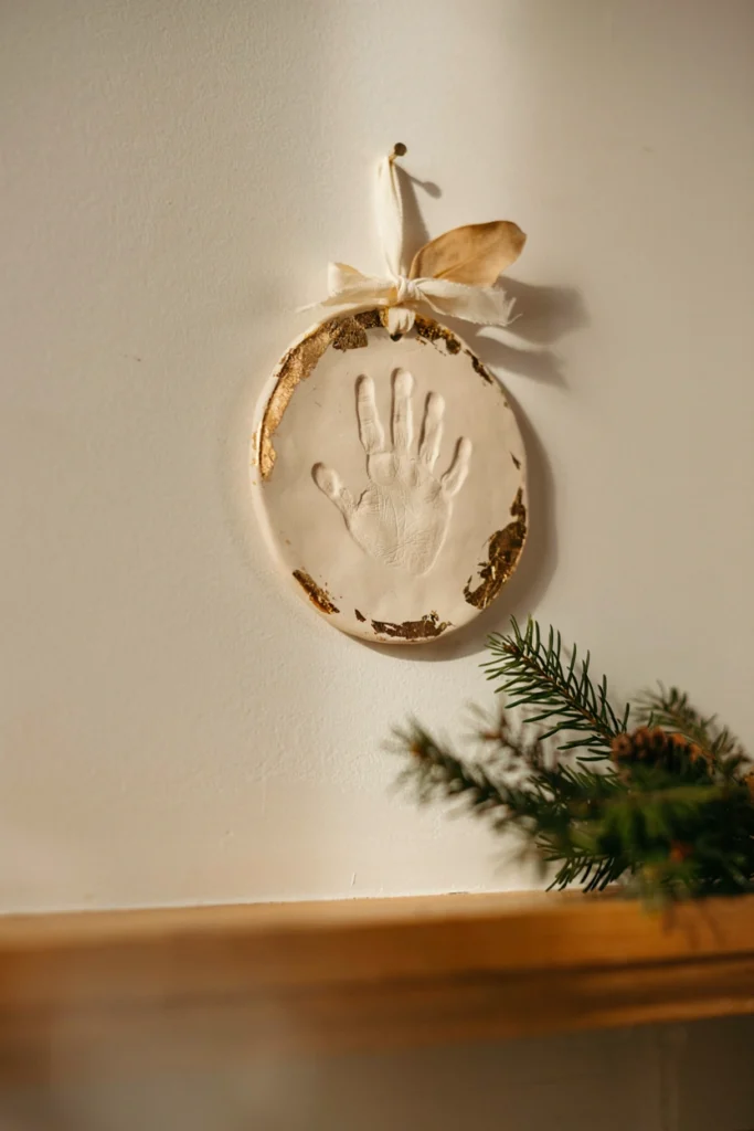 Pale tan salt dough ornament shaped like a child's handprint with the name and year painted in delicate cursive script