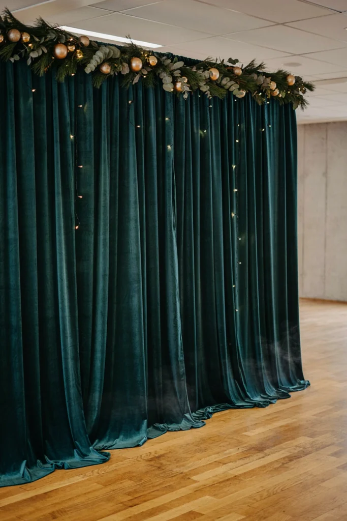 Deep green velvet drapes hung as a photo backdrop threaded with warm fairy lights