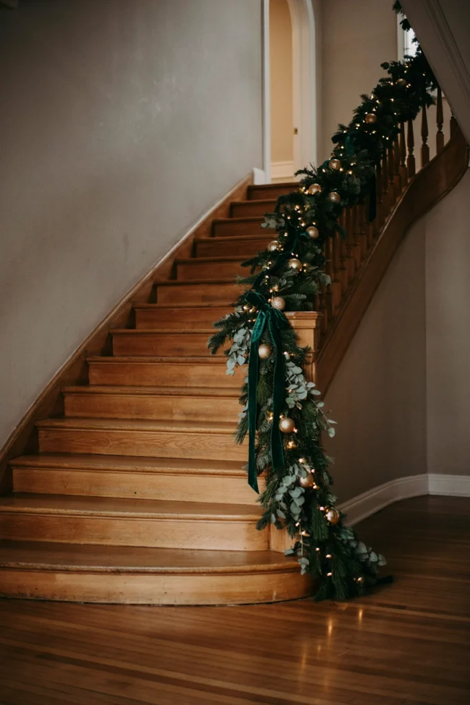 Sweeping staircase wrapped in thick garland dotted with warm white lights from top to bottom