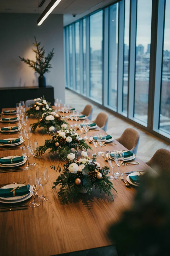 Three low, staggered centerpieces of pinecones, white candles, and greenery on a long conference table
