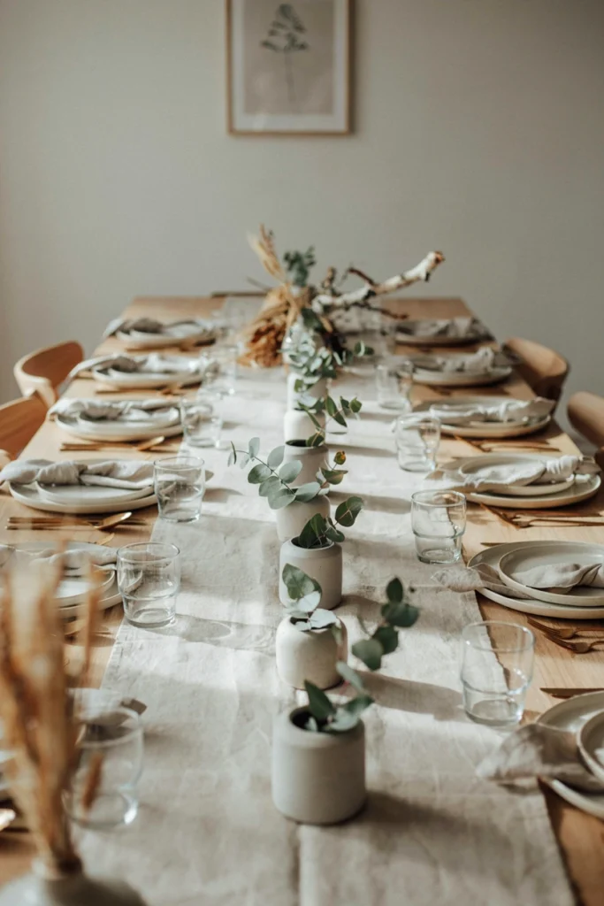 Small concrete planters filled with eucalyptus sprigs down a linen table runner with no red or green Christmas colors