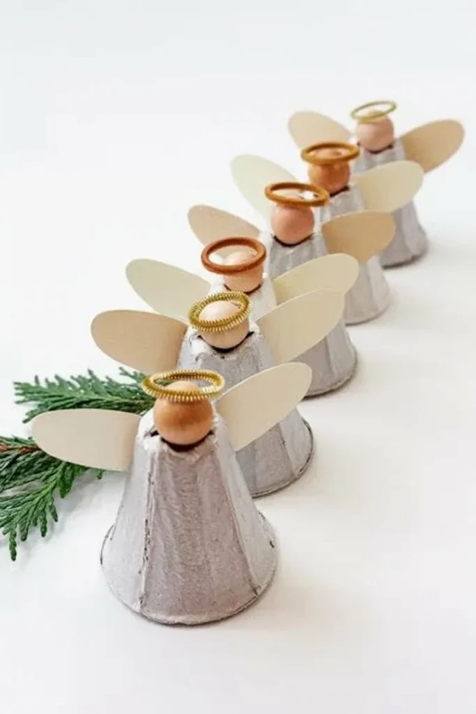Small angel figures made from painted egg carton cups with paper wings lined along a windowsill