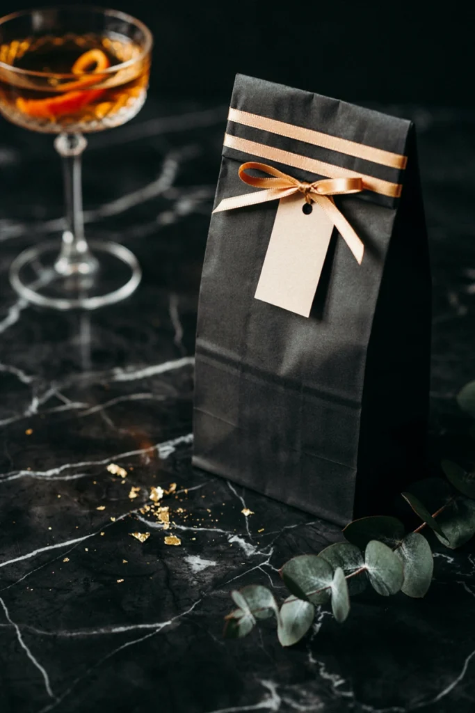 Black paper bag with thin gold foil stripes and a slim gold ribbon